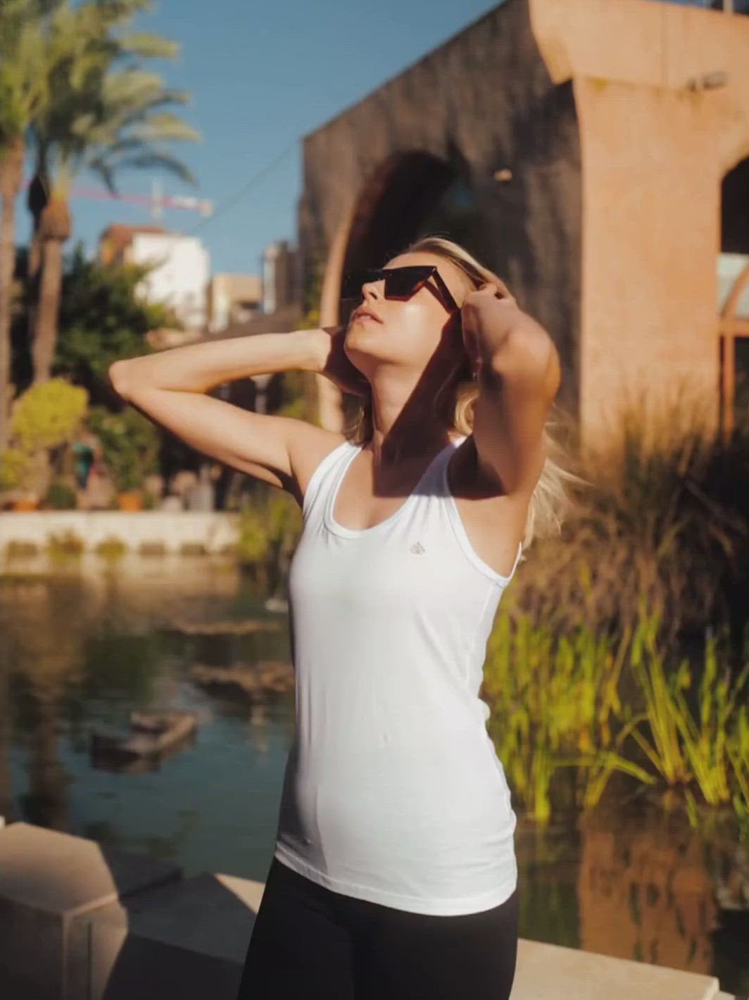 Raglan dámské tílko z biobavlny bílé žena stojí u kašny a prohazuje si vlasy při západu slunce