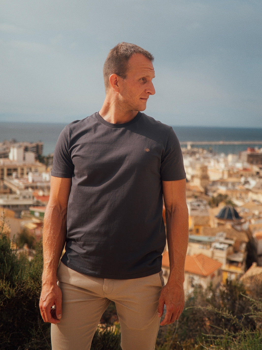 Feel pánské tričko z biobavlny s kulatým výstřihem antracitové stojící muž na kopci s pozadím města